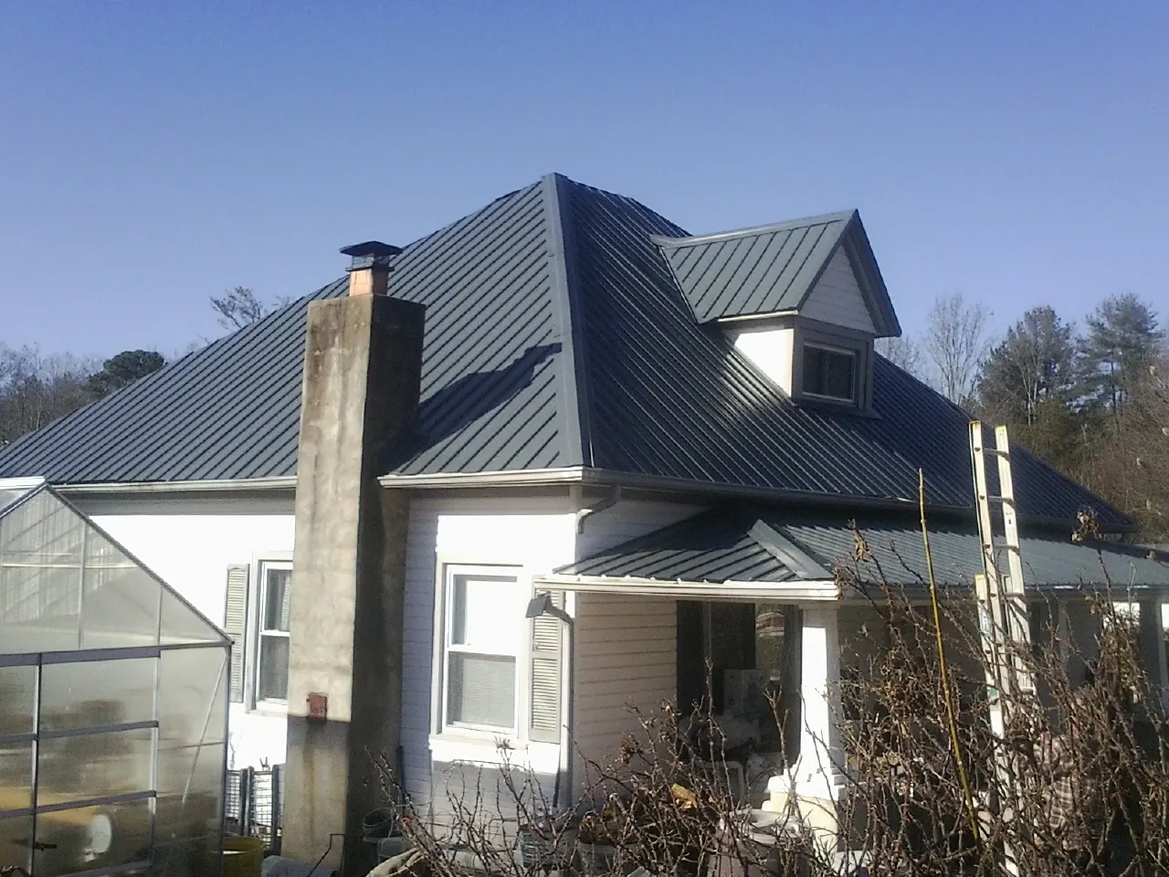 Dark blue standing seam metal roof on a white farmhouse with dormer — Slate & Tile Roof Repair by Roofing Brothers in Oakville