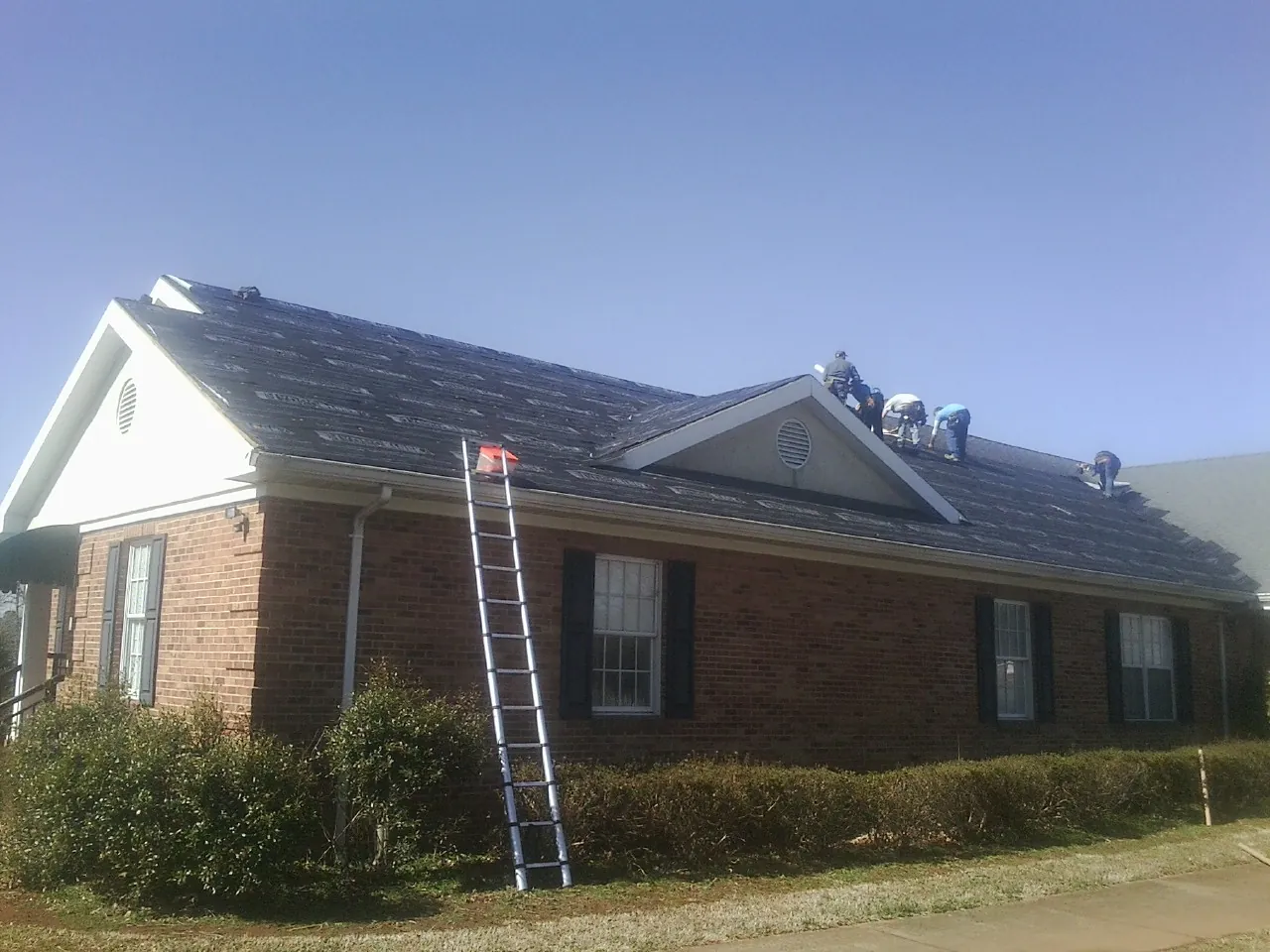 Crew tearing shingles off a brick ranch roof with a ladder set — Metal Roof Repair work by our crew in Oakville