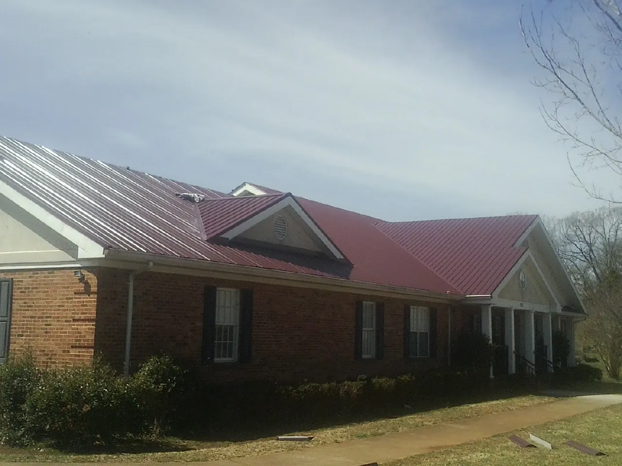 Red metal roof with gabled entries on a long brick building, from a Hail Damage Roof Repair job in Oakville